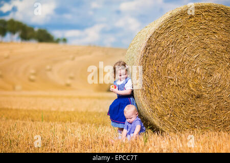 Two children, funny curly toddler girl and a little baby boy, wearing traditional German costumes playing in a field Stock Photo