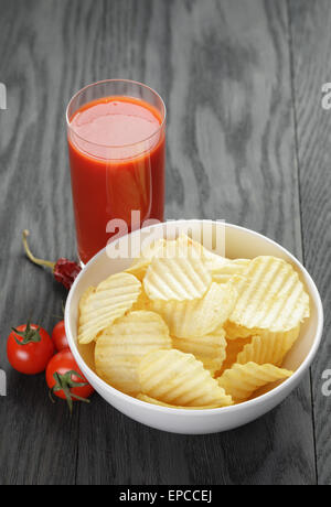 rippled organic chips in white bowl wit tomato juice on wooden table Stock Photo