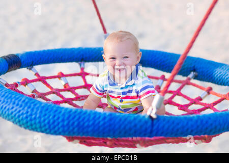 Happy laughing baby, adorable little boy enjoying a swing ride having fun on a playground in summer Stock Photo