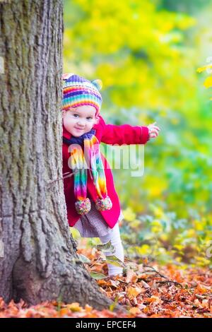 Funny little toddler girl playing with golden maple leaves in a sunny park with yellow and orange trees on a warm autumn day Stock Photo