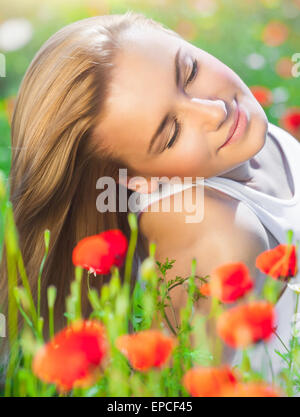 Beautiful woman with closed eyes lying down on poppy flower field, relaxation outdoors on fresh gentle floral meadow Stock Photo