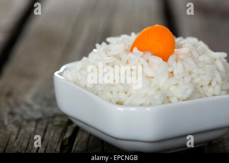 Bowl full of rice and one slice of carrot over wooden background Stock Photo