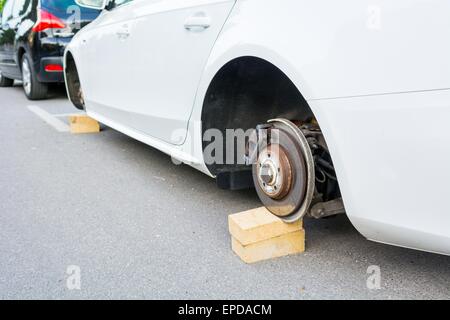 Car with stolen wheels. White vehicle left on wooden bricks. Stock Photo
