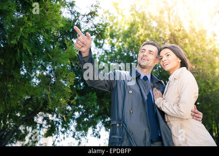 Smiling man pointing on something to his girlfriend outdoors. Trees on background Stock Photo