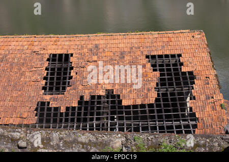 Hole in damaged tiled roof with wooden frame of a traditional building. Stock Photo