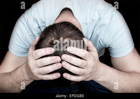 Depressed crying scared man holding his head in his hands sitting on floor over black background. Despair, depression, hopelessn Stock Photo