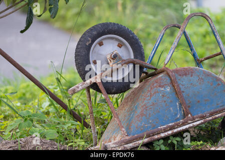 An old rusty blue wheelbarrow lying upside down in overgrown grass Stock Photo