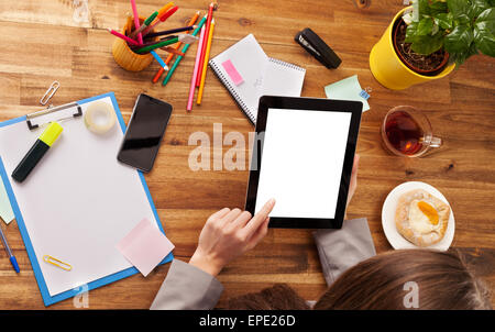 Young woman working with tablet placed on wooden desk with blank screen for text. Shot from aerial view Stock Photo