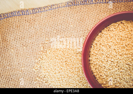 couscous grains in a brown porcelain bowl on a burlap surface Stock Photo