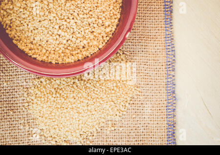 couscous grains in a brown porcelain bowl on a burlap surface Stock Photo