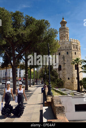 Two young women in flamenco dresses walking along Christopher Columbus Avenue with Torre del Oro Seville Stock Photo