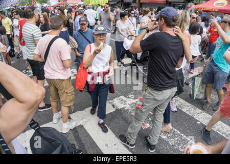 New York, USA. 17th May, 2015.  multiethnic kids & grownups eat street food & play at the annual 9th Avenue International Food Festival in Hells Kitchen neighborhood against a backdrop of midtown Manhattan. Inaugurated in 1973, the festival extends from 57th to 42nd street along Ninth Avenue in New York’s Hells Kitchen neighborhood.  Credit:  Dorothy Alexander/Alamy Live News Stock Photo