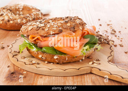 Salmon whole grain bagel on wooden kitchen board on wooden background. Traditional bagel eating. Stock Photo
