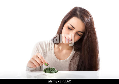 Beautiful happy healthy girl in her 20s with green dietary supplements chlorella, spirulina and wheatgrass pills on white Stock Photo