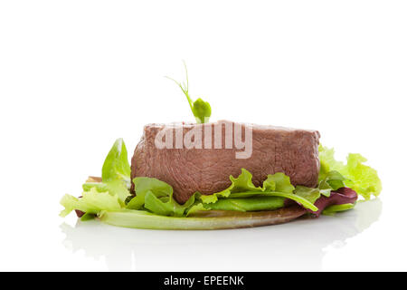 Big steak on green salad isolated on white background. Culinary beefsteak eating. Filet mignon, tenderloin steak. Red meat. Stock Photo