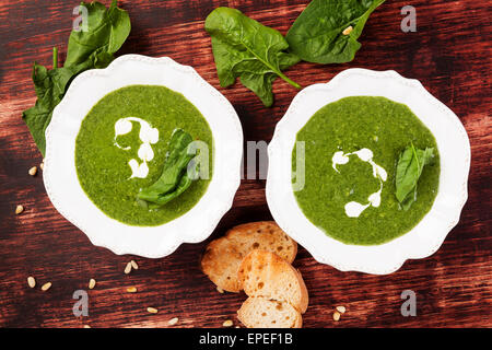 Delicious fresh spinach soup with fresh spinach leaves and bread in two vintage plates on wooden background, top view. Stock Photo