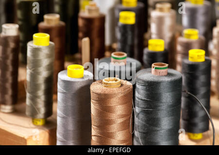Background view of various colored yarns on bobbins at a tailor or clothing design studio in shades of gray and browns Stock Photo