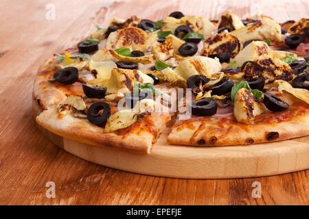 Pizza detail on wooden background. Italian cuisine, pizza with black olives, artichokes and ham. Culinary eating.