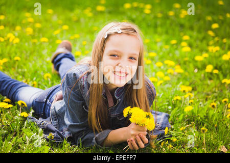 spring portrait of smiling girl lying in meadow holding bouquet of dandelions Stock Photo