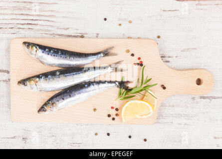 Delicious anchovies fish with peppercorns and fresh herbs on wooden chopping board on white wooden background, top view.. Stock Photo