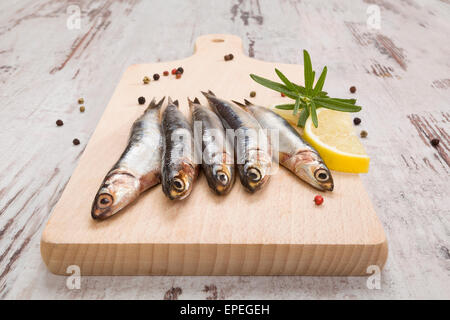 Several sardines on wooden chopping board on white wooden background, top view. Mediterranean seafood eating. Stock Photo