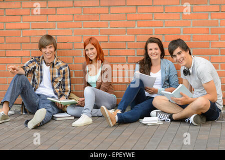 College students sitting ground by brick wall Stock Photo