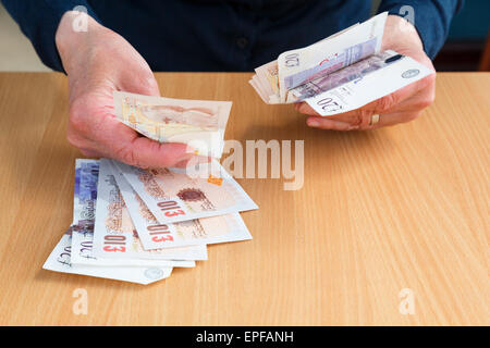 A senior person's hand holding English money in Sterling ten and twenty pound bank notes GBP to buy and pay pounds cash over a counter. England UK Stock Photo