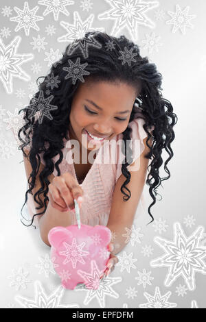 Composite image of a young girl lying on the floor putting money into a piggy bank Stock Photo