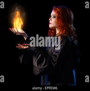 Young witch with flame isolated on black Stock Photo