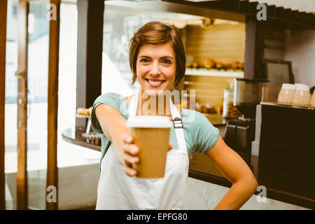 Pretty barista smiling at camera holding disposable cup Stock Photo