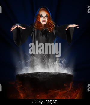 Young witch with cauldron on blue rays background Stock Photo