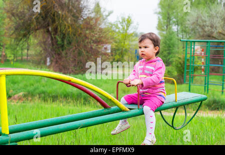 Little cute girl sits on seesaw in a sunny day Stock Photo
