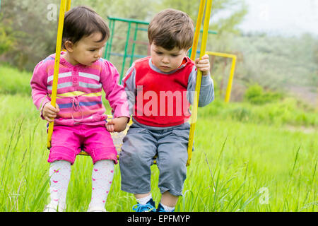 Two little kids having fun on a swing on summer day Stock Photo