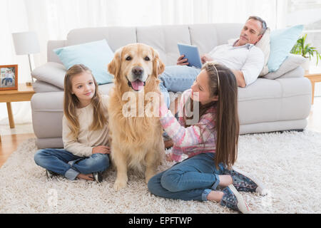Smiling sisters petting their golden retriever on rug Stock Photo