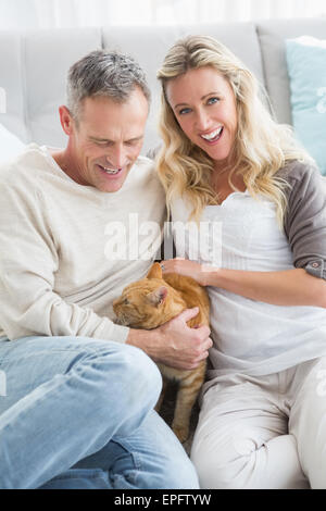 Smiling couple petting their gringer cat on rug Stock Photo