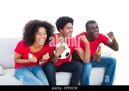 Cheering football fans in red sitting on couch Stock Photo