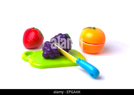 A plastic toy strawberry, mandarin orange and grapes on a cutting board being cut in half with a plastic knife. Stock Photo