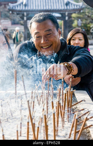Chion-in temple in Kyoto. Smiling middle ages Japanese man placing incense stick into the grey ash in an incense burner with other sticks smouldering. Stock Photo
