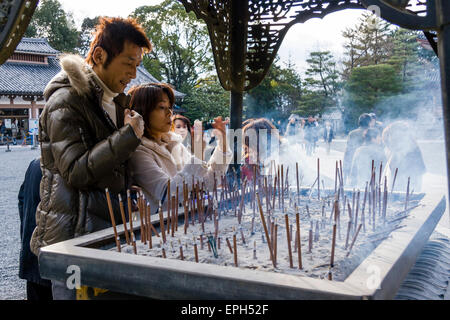 Chion-in temple in Kyoto. Family standing around incense burner praying and waving the smoke from smouldering incense, osenko, sticks over themselves. Stock Photo