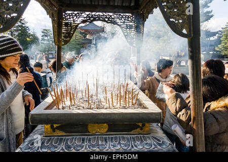 Chion-in temple in Kyoto. People standing around incense burner praying and waving the smoke from smouldering incense, osenko, sticks over themselves. Stock Photo