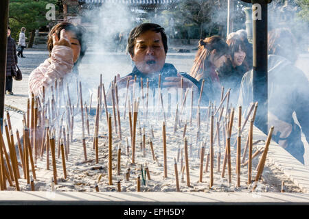 Chion-in temple in Kyoto. Man standing at incense burner praying and waving the smoke from smouldering incense, osenko, sticks over himself. Stock Photo