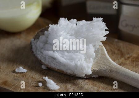A wooden spoonful of coconut oil, ready and waiting to be cooked with. Onion in background Stock Photo