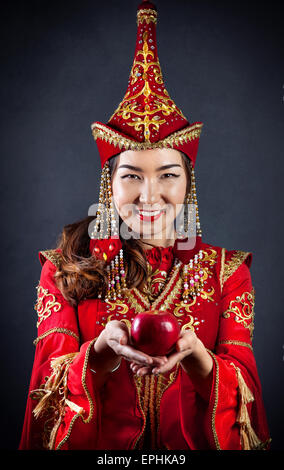 Woman in red national Kazakh costume holding red apple at grey background Stock Photo
