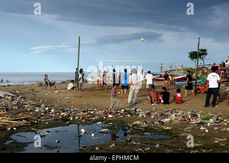 Men playing a game of volleyball on beach covered in plastic trash and other garbage in Sumatra, Indonesia Stock Photo