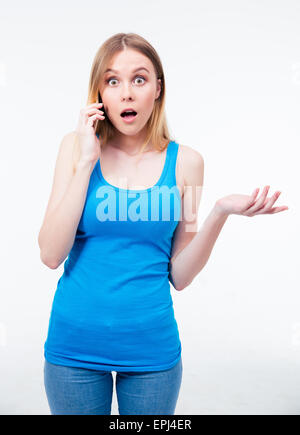 Surprised woman talking on the phone over gray background and looking at camera Stock Photo