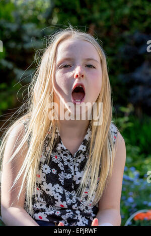 Blonde 8 year old girl sitting in a garden shouting at the photographer Stock Photo