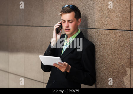 Young man with tablet computer calling on phone Stock Photo