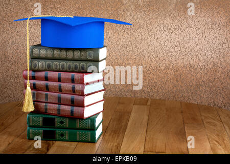 Graduation mortarboard on top of stack of books on abstract background of wall Stock Photo