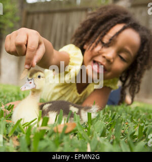 A young girl lying on the grass stroking the head of a duckling. Stock Photo
