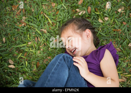 A girl lying on her side with her knees drawn up laughing. Stock Photo